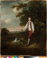 Portrait of a youth holding a cricket bat and ball with his pet black and white springer spaniel in a clearing by a wooded landscape